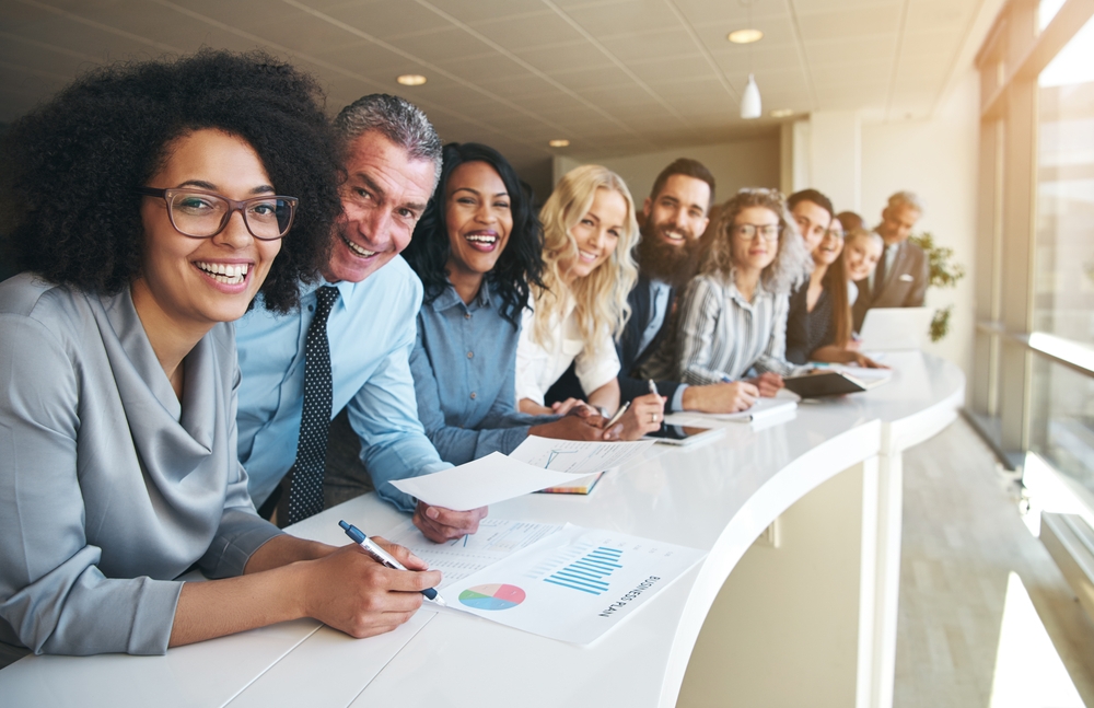 Smiling colleagues gather around a table with reports and pens on the table.