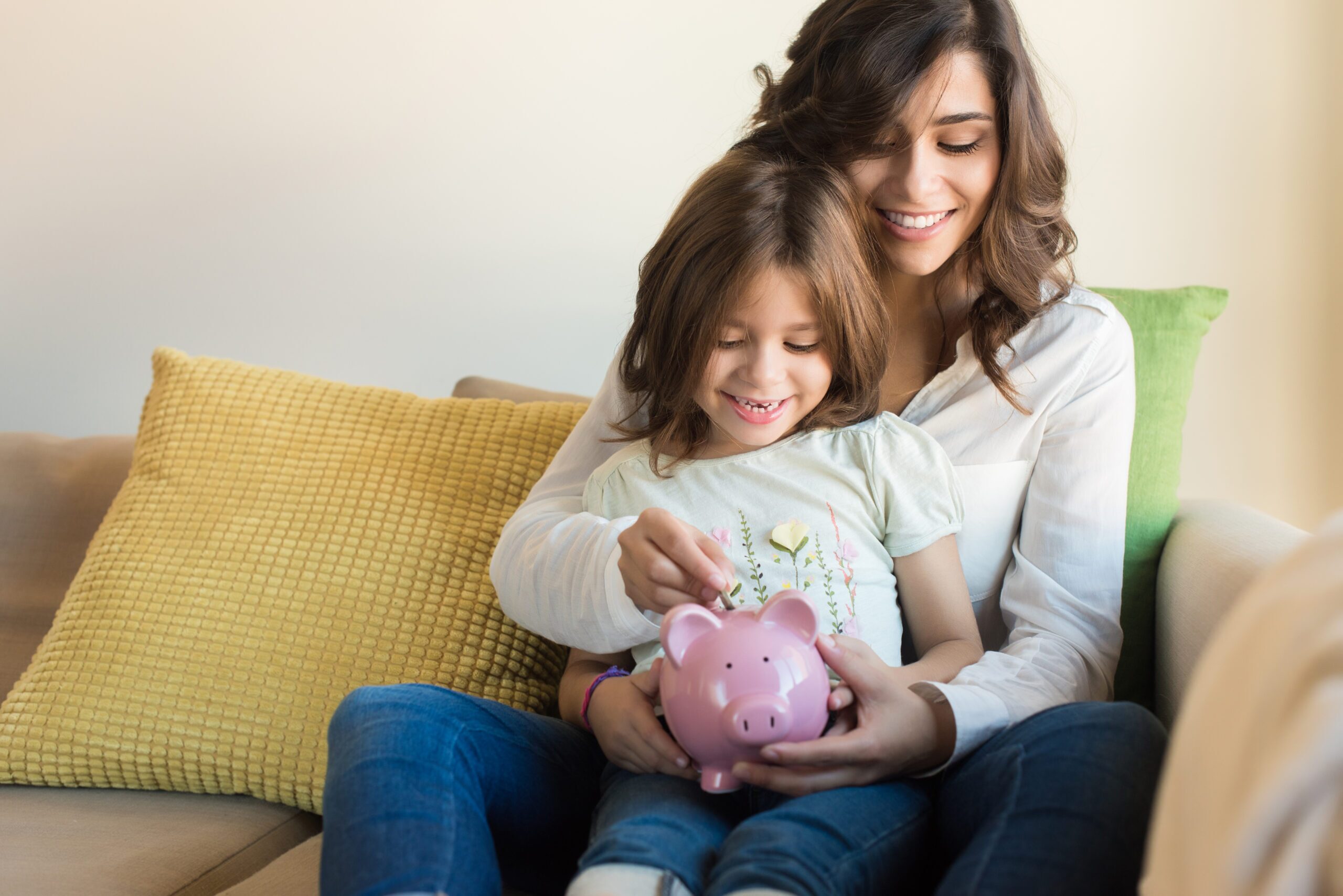 mom holds a baby on her knees and the baby holds a pig saving jar.