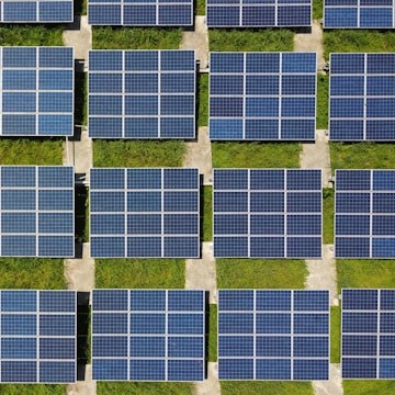 Aerial view of rows of solar panels on a green field, arranged neatly on rectangular platforms, conveying a sense of clean energy and sustainability.