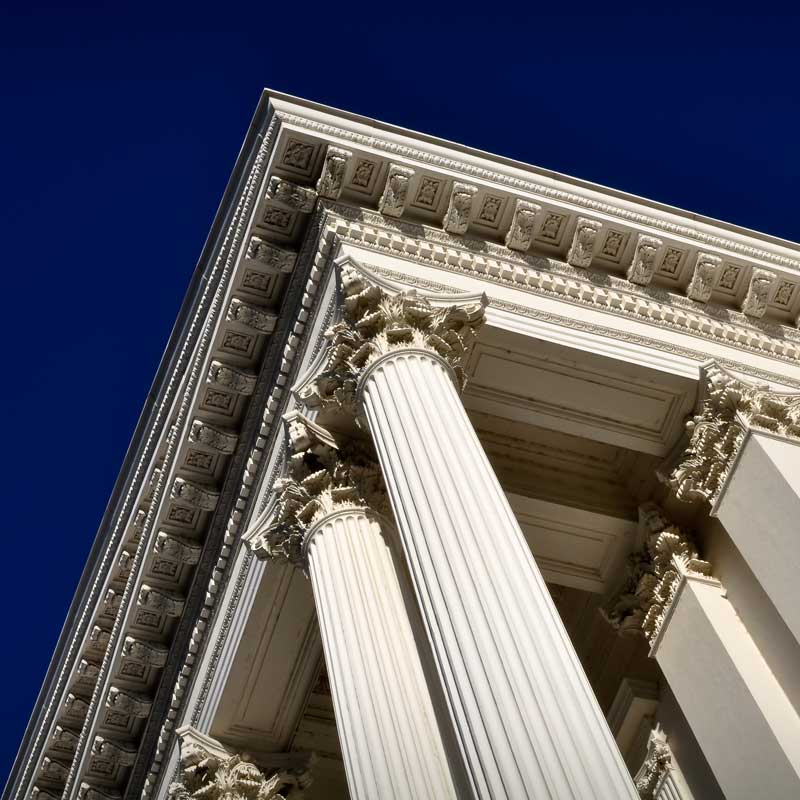 Close-up of a classical building with tall, ornate Corinthian columns and intricate architectural details, set against a clear blue sky.