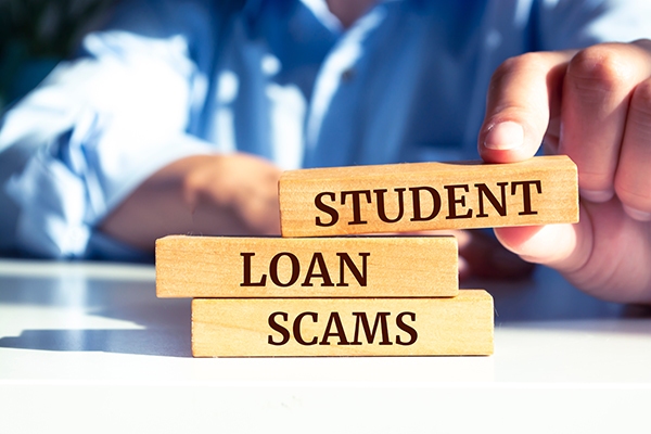 Fingers stacking wooden blocks that read "Student Loan Scams"