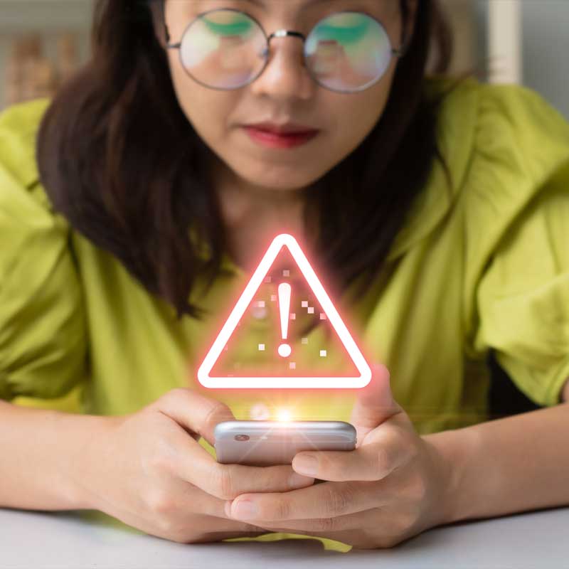 A girl holds a cellphone in her hands and a alert sign is on top of the cellphone