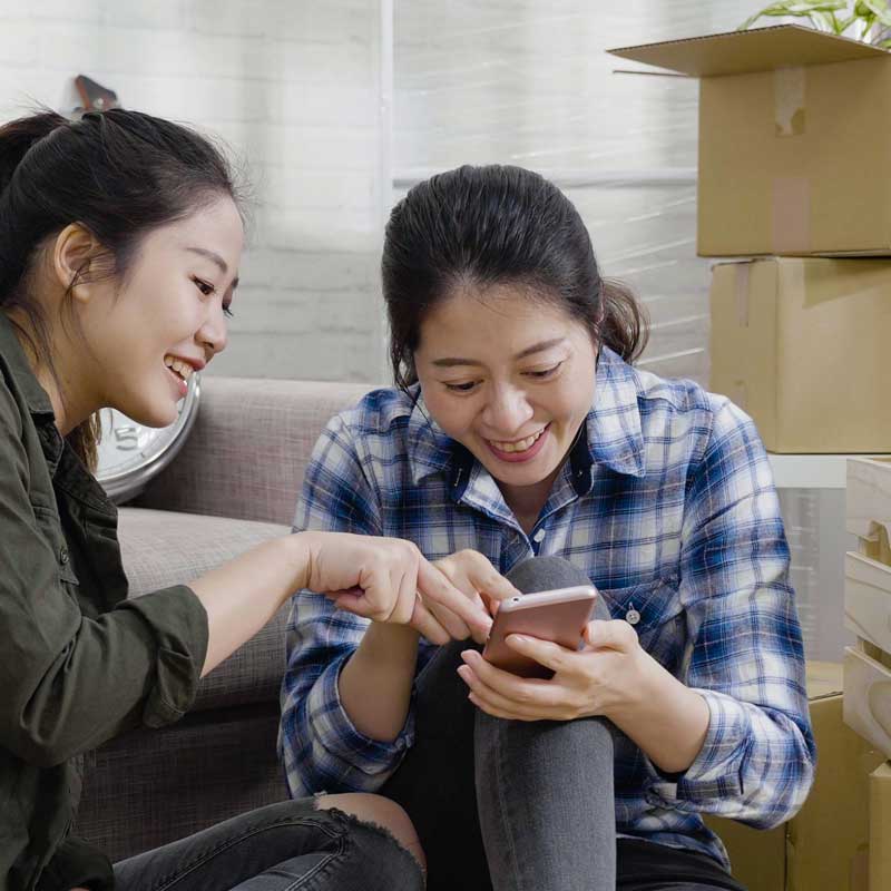 A girl is checking her cell phone and talking to another person nearby