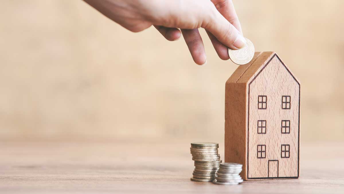 Hand putting a coin into a toy bank shaped like a house