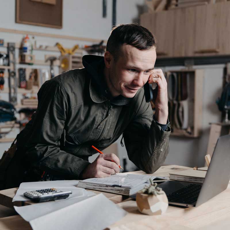 A man holds a phone on his ear and makes note on his notebook